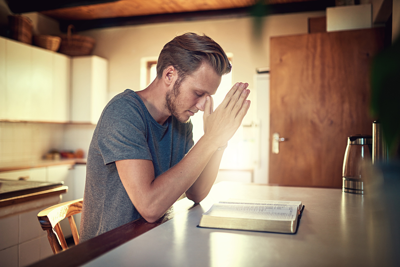 Shot of a devoted young man clasping his hands in prayer over an open Bible